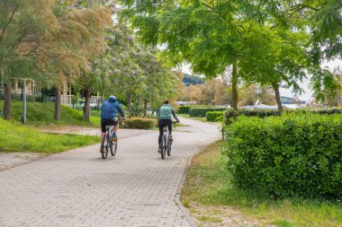 Tar, Hırvatistan - 23 Mayıs 2025: İki kişi Adriyatik kıyısında çiçek açan ağaçlar ve yeşilliklerle çevrili manzaralı bir patika boyunca huzurlu bir bisiklet yolculuğunun keyfini çıkarıyor.