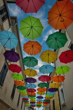 Tarihi binalar arasında yüzen renkli gökkuşağı şemsiyeleri büyüleyici Akdeniz şehir ortamında sanatsal sokak dekorasyonu yaratıyor..