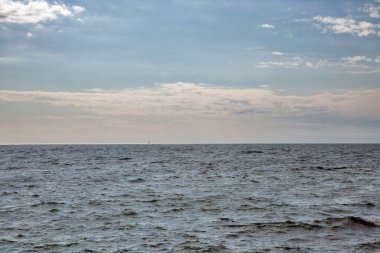 Karanlık su yüzeyinde hafif dalgalarla sakin deniz manzarası parçalı bulutlu mavi gökyüzü altında beyaz kabarık bulutlar altında uzak ufuklara kadar uzanıyor..