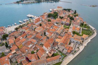 Hırvatistan 'ın Istria kıyısındaki Porec Eski Kenti ve Euphrasian Bazilikası' nın havadan görünüşü. Kırmızı kiremitli çatılar ve tarihi binalar, yakındaki marinaya sahip Adriyatik kıyı şeridi boyunca dinleniyor..