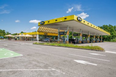 Draganiç, Hırvatistan - 31 Mayıs 2025: Jana markalı şemsiyeler, dekoratif inek heykeli ve güneşli bir günde içeceklerin keyfini çıkaran müşterilerle birlikte açık hava yemek alanının yer aldığı çağdaş Tifon benzin istasyonu.