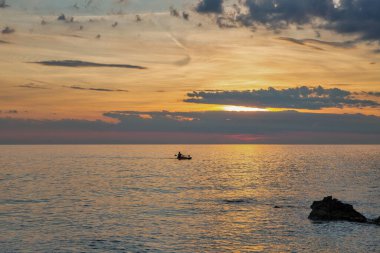 Hırvatistan 'ın Istria kentinde canlı bir günbatımı sırasında küçük bir tekne sakin Adriyatik Denizi' nde huzur içinde sürükleniyor. Sıcak renkler ve dramatik bulutlar sakin bir deniz manzarası yaratıyor..