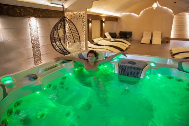 Orta yaşlı bir kadın, sıcak, aydınlık bir jakuzide, yumuşak bir ışık ve sakin bir atmosferle çevrili, huzurlu bir şekilde banyo yapıyor..