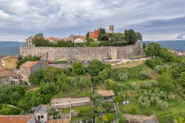 Hırvatistan 'ın Istria kentindeki Ortaçağ' a ait Motovun kasabasının insansız hava aracı görüntüsü, yeşil ormanlar, taş duvarlar ve kırmızı çatı evleriyle çevrili..