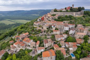 Hırvatistan 'ın Istria kentindeki Ortaçağ' a ait Motovun kasabasının insansız hava aracı görüntüsü, yeşil ormanlar, taş duvarlar ve kırmızı çatı evleriyle çevrili..