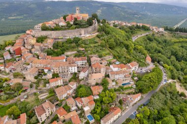 Hırvatistan 'ın Istria kentindeki ortaçağ dağ kasabasının insansız hava aracı görüntüsü, yeşil ormanlar, taş duvarlar ve çatı evleriyle çevrili.