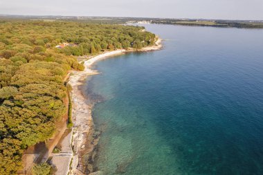 Hırvatistan 'ın Istria kentindeki Istria kentindeki ormanlık Lanterna yarımadası tatil beldesinin hava gün batımı drone görüntüsü, etrafı oteller ve eğlence tesisleriyle çevrili Adriyatik sularıyla çevrili. Arkaplanda Cervar-Porat.