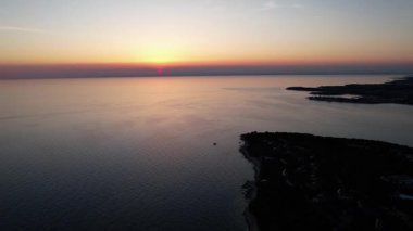 Hırvatistan 'ın Istria kentindeki kayalık bir günbatımı sahil şeridinin hava aracı görüntüsü, kristal berrak turkuaz su, sörf dalgaları ve kayalıkların üzerindeki yemyeşil orman. Arka planda Novigrad.