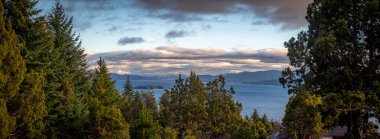 Arjantin 'in Bariloche kentindeki ormanlarla çevrili Nahuel Huapi Gölü' nün güzel günbatımı manzarası, arka plandaki adalar ve dağlar..