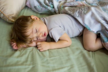 Tatlı uyuyan bebek. Çocukların gündüz uykusu. Küçük beyaz çocuk büyük bir yatakta, battaniyenin altında uyuyor. Güzel uyuyan bir bebeğin yakın plan portresi. Sarışın çocuk.. 