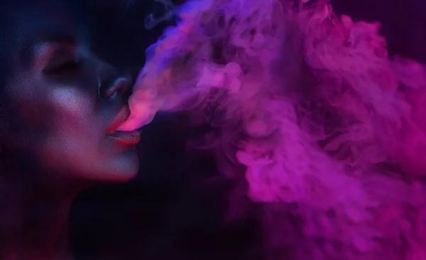 女性肖像简介 漂亮性感的年轻女人在夜总会里喷出烟熏 在俱乐部抽烟的女孩蓝色的神秘之光夜生活 图库照片