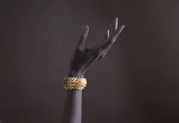Black woman\'s hand with gold jewelry. Oriental Bracelet on a black painted hand. Gold Jewelry and luxury accessories on black background closeup. High Fashion art concept