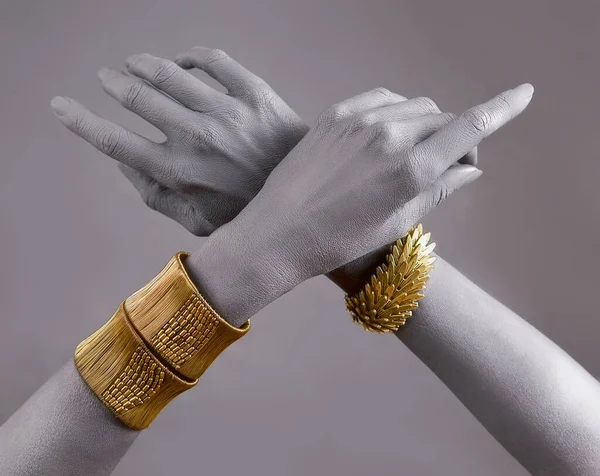 Gray woman's hands with gold jewellery. Oriental Bracelets on a painted hand. Gold Jewelry and luxury accessories on Gray background closeup. High Fashion art concept