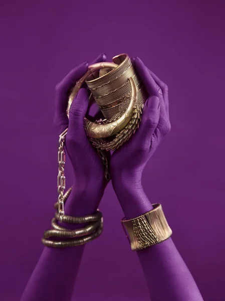 magenta woman\'s hands with gold jewelry. Oriental Bracelets on a purple painted hand. Gold Jewelry and luxury accessories on violet background closeup. High Fashion art concept