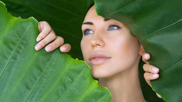 Beautiful Sexy Woman face with Natural nude make-up on a tropical leaf background. Healthy life. Woman and the leaves. Pure natural cosmetic and wellness concept. Purity and skincare. Space for text