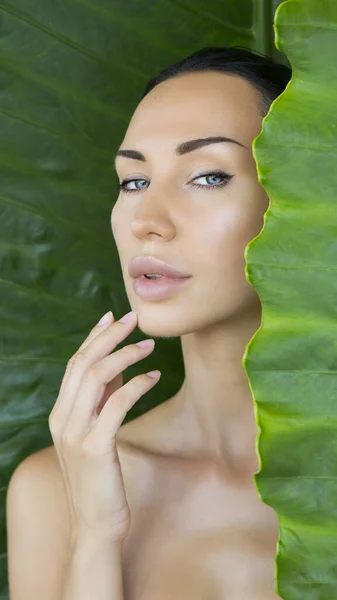 Beautiful Sexy Woman face with Natural nude make-up on a tropical leaf background. Healthy life. Woman and the leaves. Pure natural cosmetic and wellness concept. Purity and skincare. Space for text