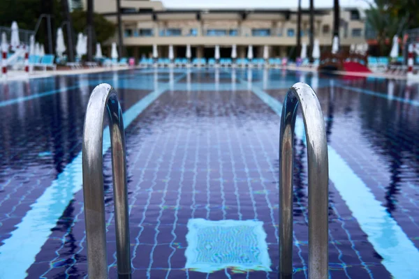 Bulanık yüzme havuzlu metal havuz merdiveni ve bulutlu bir günde arka planda kapalı şemsiyeler.