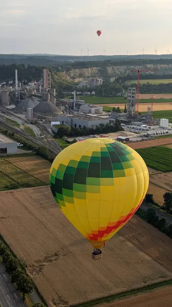Arka planda çimento fabrikası olan bir arazide uçan sıcak hava balonu.