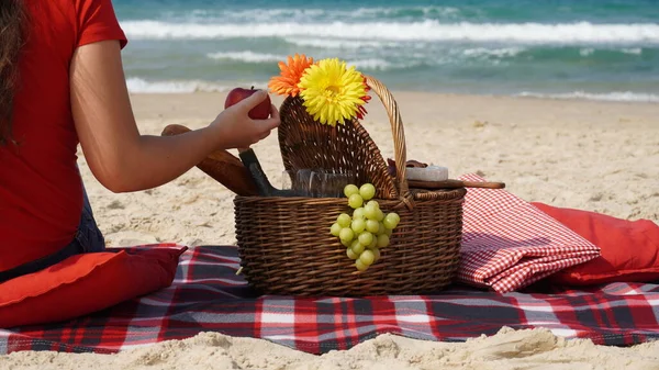 Young girl enjoying picnic on the beach. Summertime relaxation and recreation concept. Blanket with fruits on sandy beach