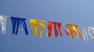 Mavi gökyüzüne asılı beyaz, mavi, sarı ve kırmızı çizgili kurdele süslemesi