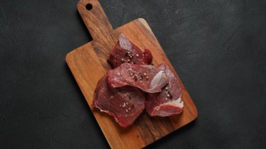 Koyu arkaplanda tahtadan yapılmış taze et. Birkaç parça çiğ et.