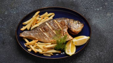 Grilled fish dorado in a plate with chips and lemon and herbs