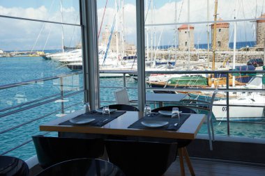 Arka planda Mandraki Limanı 'ndaki Restoran İçişleri ve Ortaçağ Değirmenleri, Rodos Adası, Yunanistan