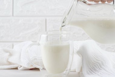 Kadın kavanozdan bardağa süt döküyor.