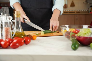 Sebze salatası yapan kadın. Ahşap kesme tahtasındaki salatalıkları kesen ellerin yakın çekimi.