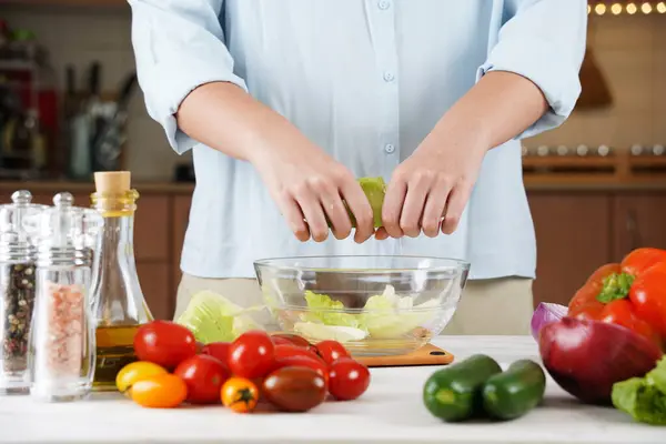 オーガニック野菜でいっぱいのテーブルに新鮮なサラダを作る女性の手の写真を閉じる — ストック写真