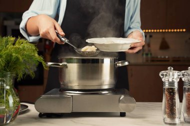 Bir kepçe dolusu haşlanmış hamur köftesi olan bir kadın. Kapaklı bir tencerede hamur tatlısı hazırlıyorum.