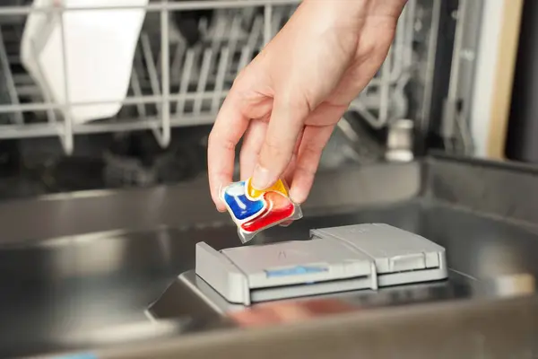 Female hand put dishwasher detergent tablet in open dish washing machine