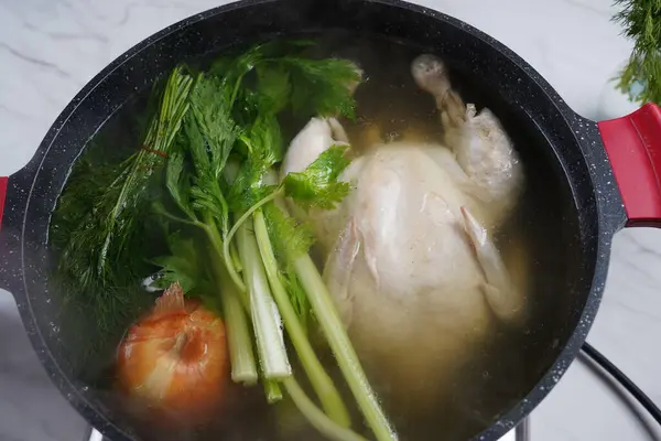 Chicken soup, chicken broth, with whole chicken and vegetables in a pot. Healthy food concept