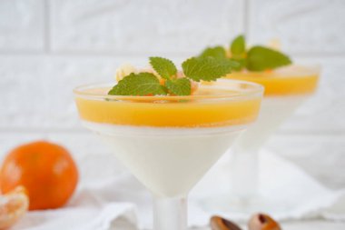 Küçük porsiyonlu vazoda mandalina katmanlı vanilyalı panna cotta ve şarap kadehlerinde meyve parçaları. Lezzetli İtalyan tatlısı.