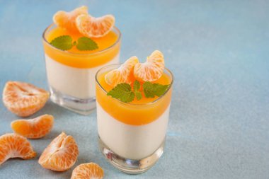 Küçük porsiyonlu vazoda mandalina katmanlı vanilyalı panna cotta ve şarap kadehlerinde meyve parçaları. Lezzetli İtalyan tatlısı.