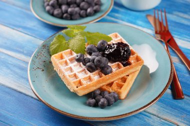 Yaban mersini reçelli lezzetli waffle 'lar ve ahşap masada taze meyveler.