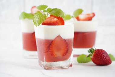 Küçük porsiyonlu vazoda çilek katmanlı vanilyalı panna cotta ve şarap kadehlerinde meyve parçaları. Lezzetli İtalyan tatlısı.