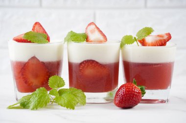 Küçük porsiyonlu vazoda çilek katmanlı vanilyalı panna cotta ve şarap kadehlerinde meyve parçaları. Lezzetli İtalyan tatlısı.