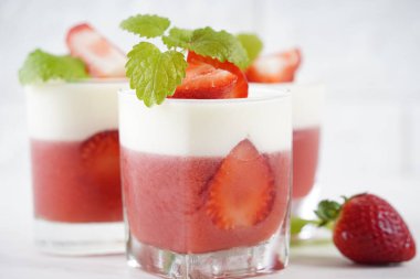 Küçük porsiyonlu vazoda çilek katmanlı vanilyalı panna cotta ve şarap kadehlerinde meyve parçaları. Lezzetli İtalyan tatlısı.