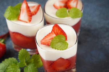 Küçük porsiyonlu vazoda çilek katmanlı vanilyalı panna cotta ve şarap kadehlerinde meyve parçaları. Lezzetli İtalyan tatlısı.