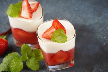 Küçük porsiyonlu vazoda çilek katmanlı vanilyalı panna cotta ve şarap kadehlerinde meyve parçaları. Lezzetli İtalyan tatlısı.