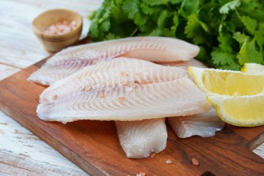 Fresh tilapia fish fillet sliced for steak or salad with herbs spices and lemon