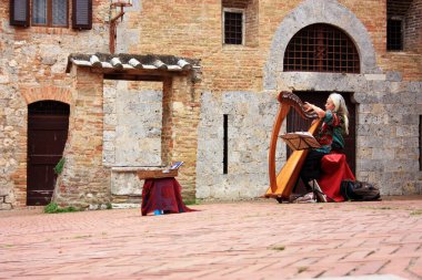 Büyülü kadın İtalya 'nın romantik Toskana kasabası San Gimignano' da antik bir meydanda arp çalıyor.
