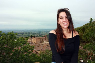 San Gimignano panoramasının önündeki genç esmer kadın. Ortaçağ Toskana şehrinde taş ve İtalya 'da kırmızı tuğlalar.