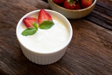 Strawberry yogurt in a wooden bowl with mint and fresh strawberry on wooden background. Health food concept.	