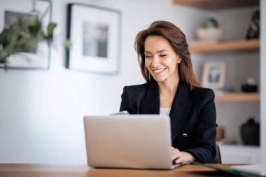 Çekici bir iş kadınının ev ofisinde çalışırken dizüstü bilgisayar kullanması. Ceket giyen kendinden emin bir kadın.. 