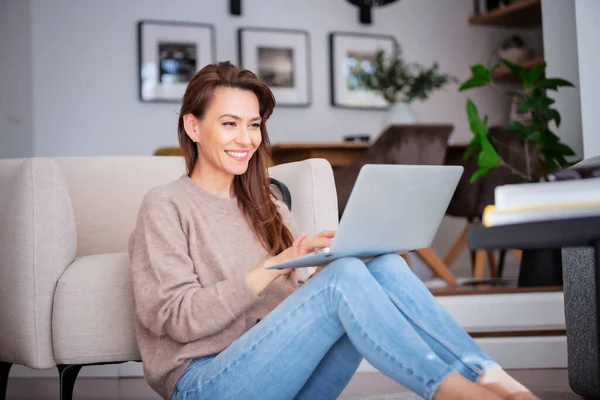 一个漂亮的中年妇女坐在地板上 同时使用笔记本电脑 穿着休闲装的漂亮女人 — 图库照片