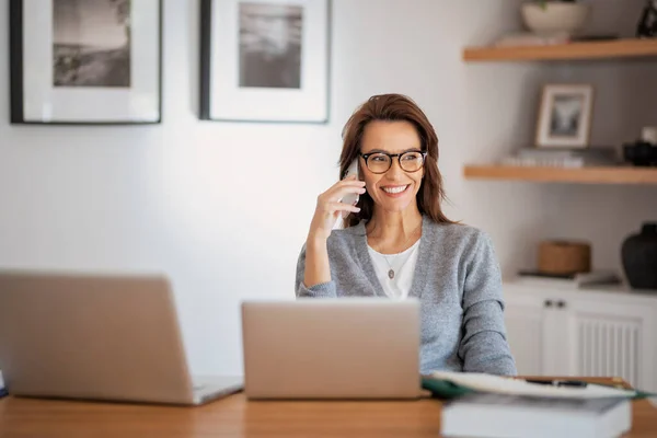 自宅から仕事をしながらアイウェアやカジュアルな服を着た魅力的な女性 ノートパソコンを使って電話をかけるビジネスウーマン 内務省 — ストック写真