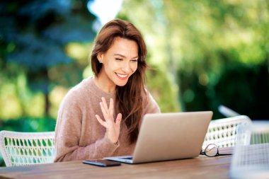 Balkonda dizüstü bilgisayarı olan ve dizüstü bilgisayar kullanan kendinden emin orta yaşlı bir kadın. Çekici bir kadın video görüşmesi sırasında elini sallıyor.. 