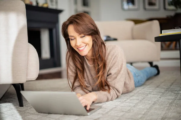 自宅でリラックスしながら ノートパソコンやインターネットで閲覧を使用して幸せな女性の完全な長さのショット セーターと青いジーンズを着た魅力的な女性 — ストック写真